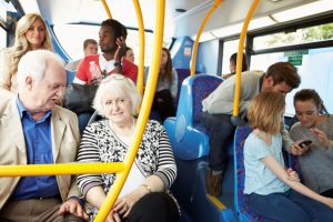 Image showing 8 diverse people riding a bus, including a white senior couple, a young black man listening to headphones, and a young family