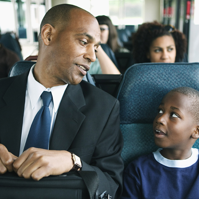 A Black dad and son looking at each other on a bus.