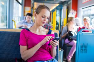 A woman in a bright pink top looking at her smartphone on a bus