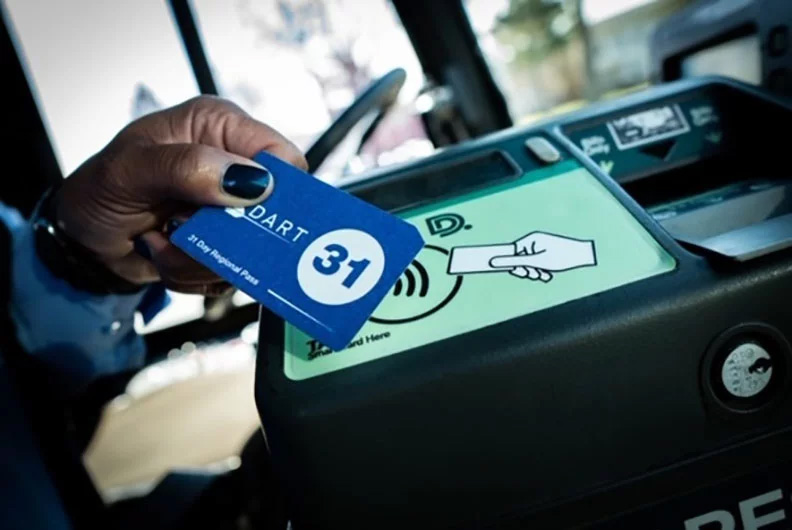 A hand of an African-American person with pretty black nailpolish holding a blue Dart card up to a card reader