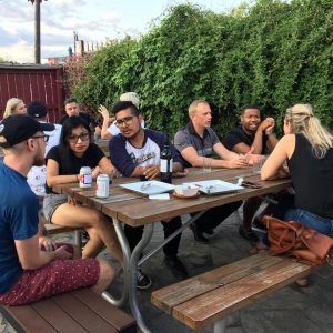 A diverse group of people talking with each other sitting at a picnic table on an outdoor patio