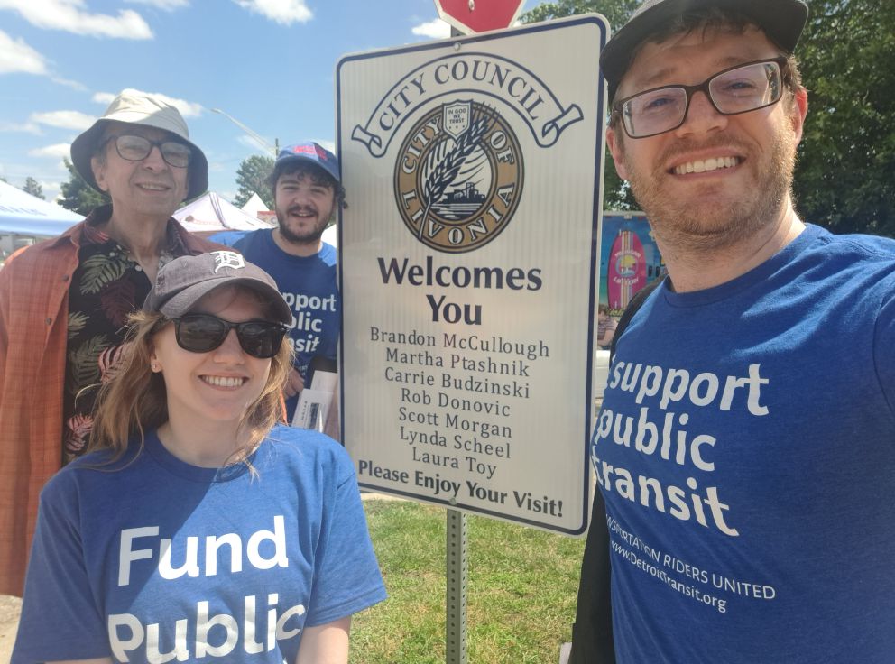 Joel, Makenna, and TRU volunteers posing with a City of Livonia sign