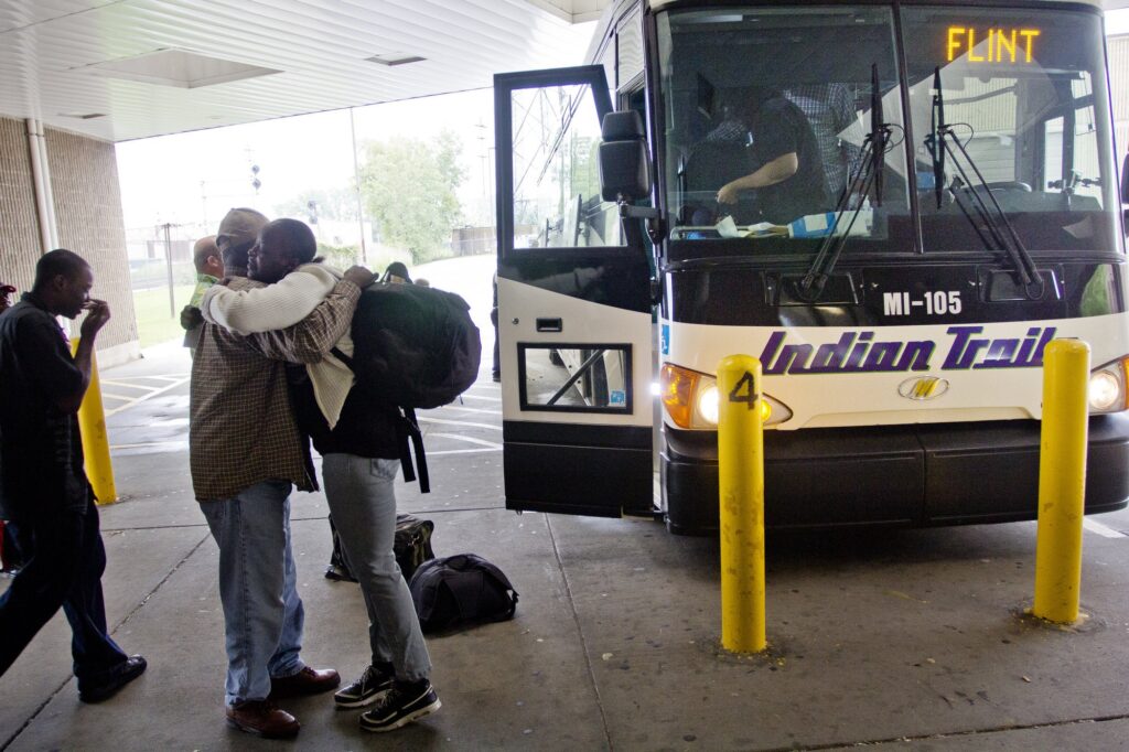 Two people hug in front of Indian Trails bus at Detroit Bus Depot, headed to Flint
