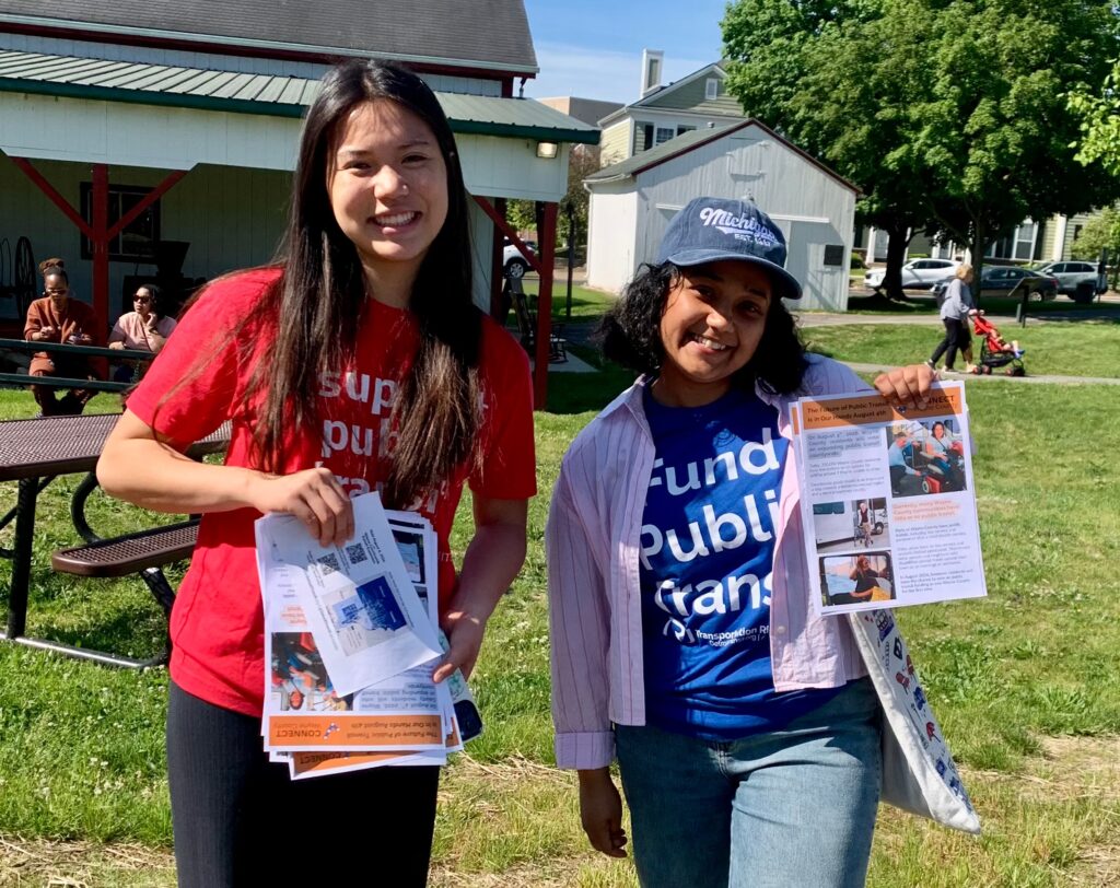 Two smiling people holding flyers and wearing transit-related shirts.
