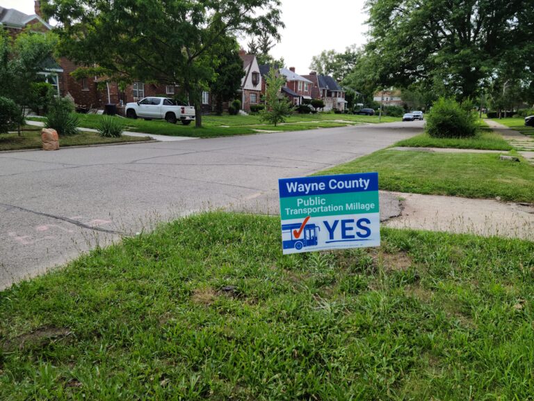 A yard sign saying "Wayne County Public Transit Millage, vote yes" with a bus and a checkmark