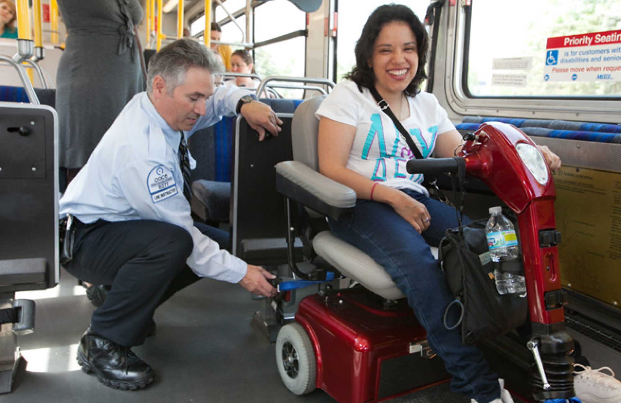 Woman in wheelchair scooter being buckled into bus by bus driver
