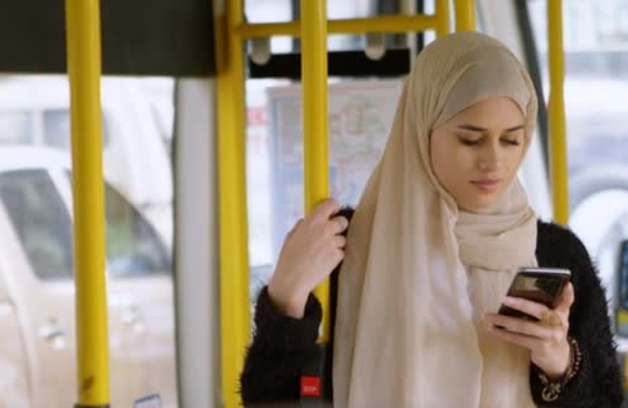 Young woman wearing a hijab, looking at a smartphone on a bus