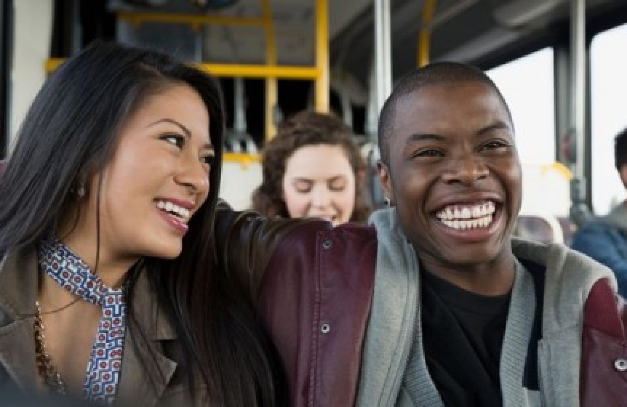 A black man and a brown woman smiling and laughing on a bus