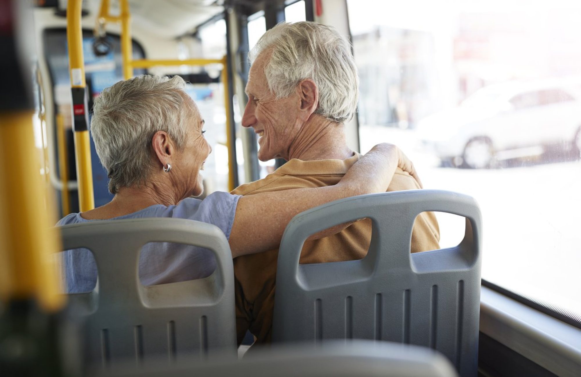 Two older people on a bus, smiling and hugging